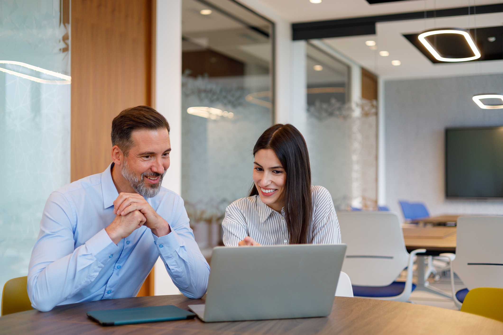 Man and woman smiling, collaborating at a laptop in modern office