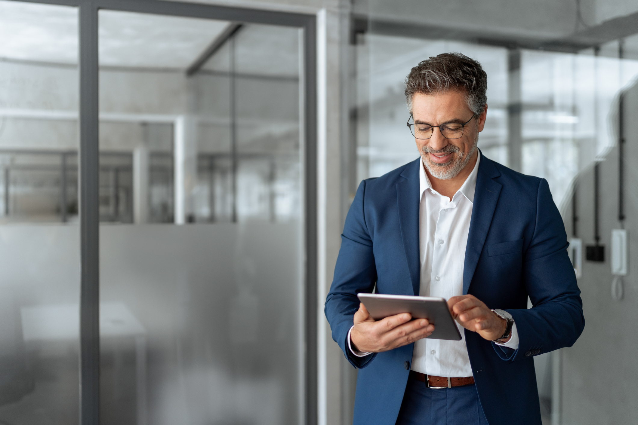Man in blue suit smiling while using a tablet in an office