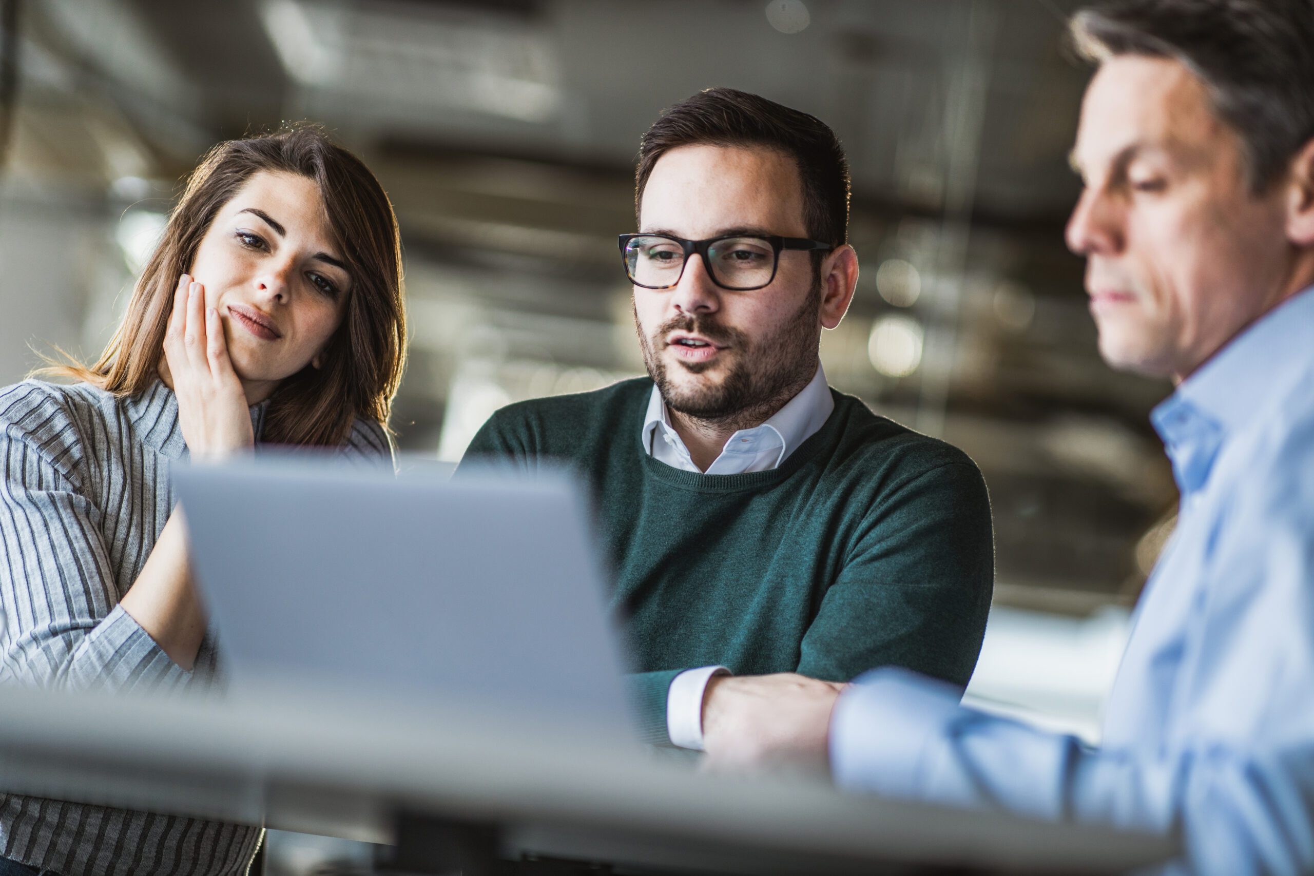 Three people engaged in discussion while viewing a laptop
