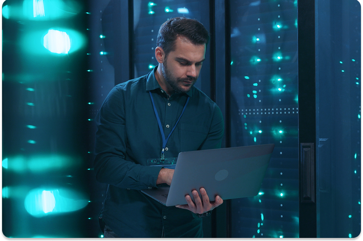 Person using a laptop in a server room, focused and analyzing data