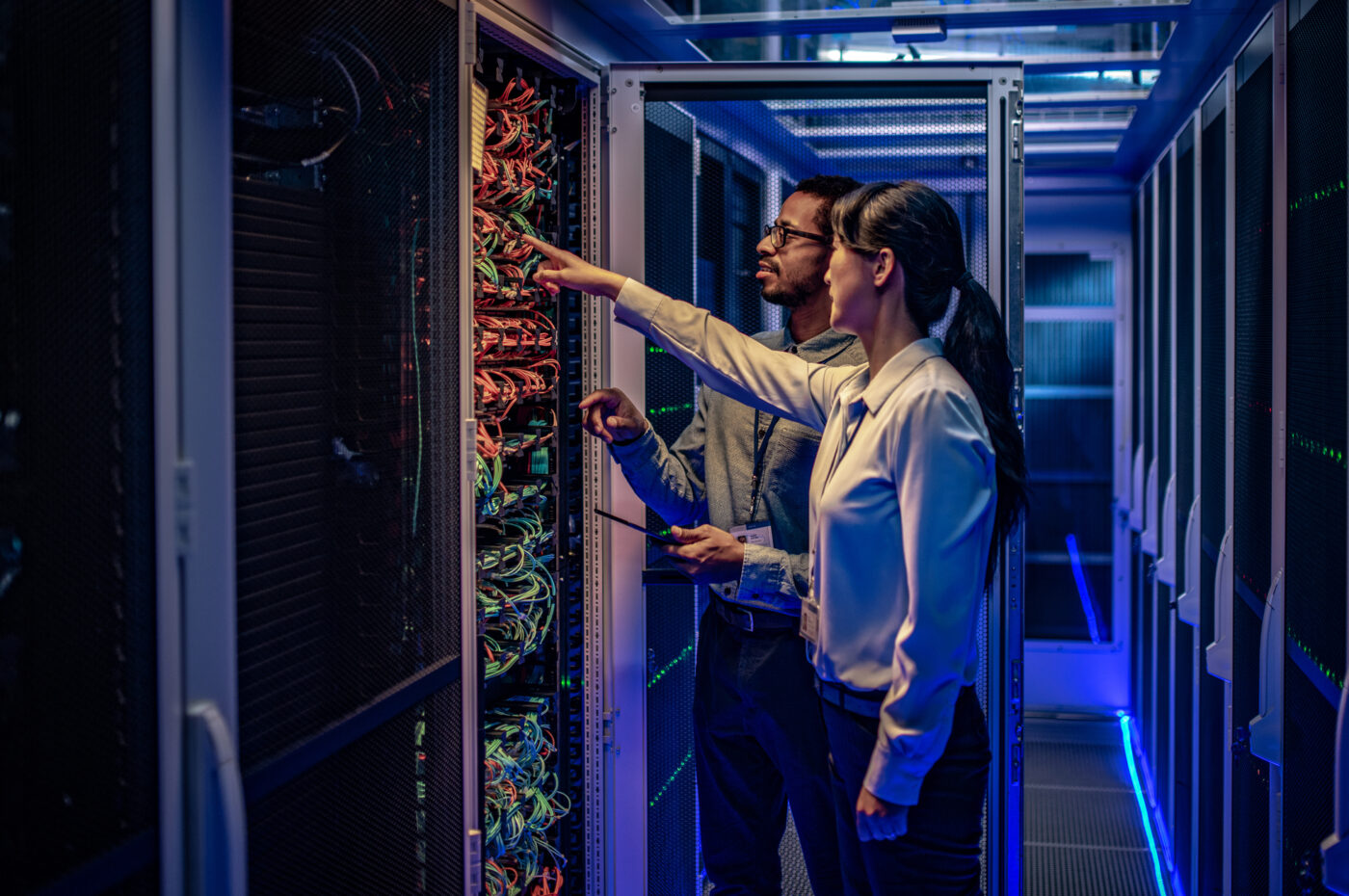 Two people in a server room, pointing and discussing cables