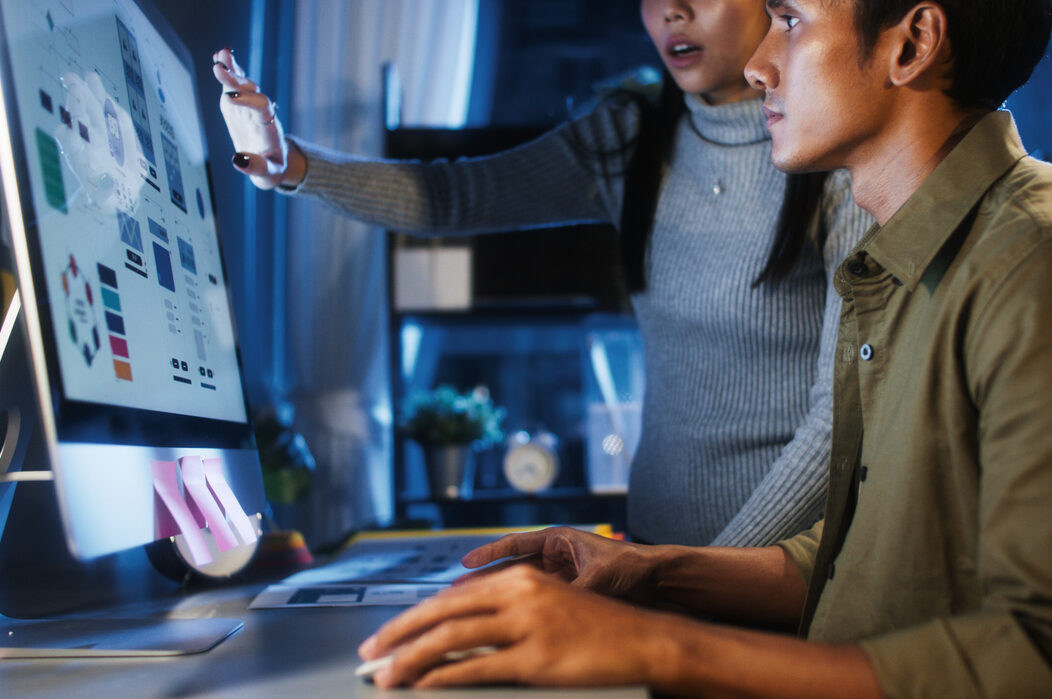 Two people reviewing design mockups on a computer screen in an office setting