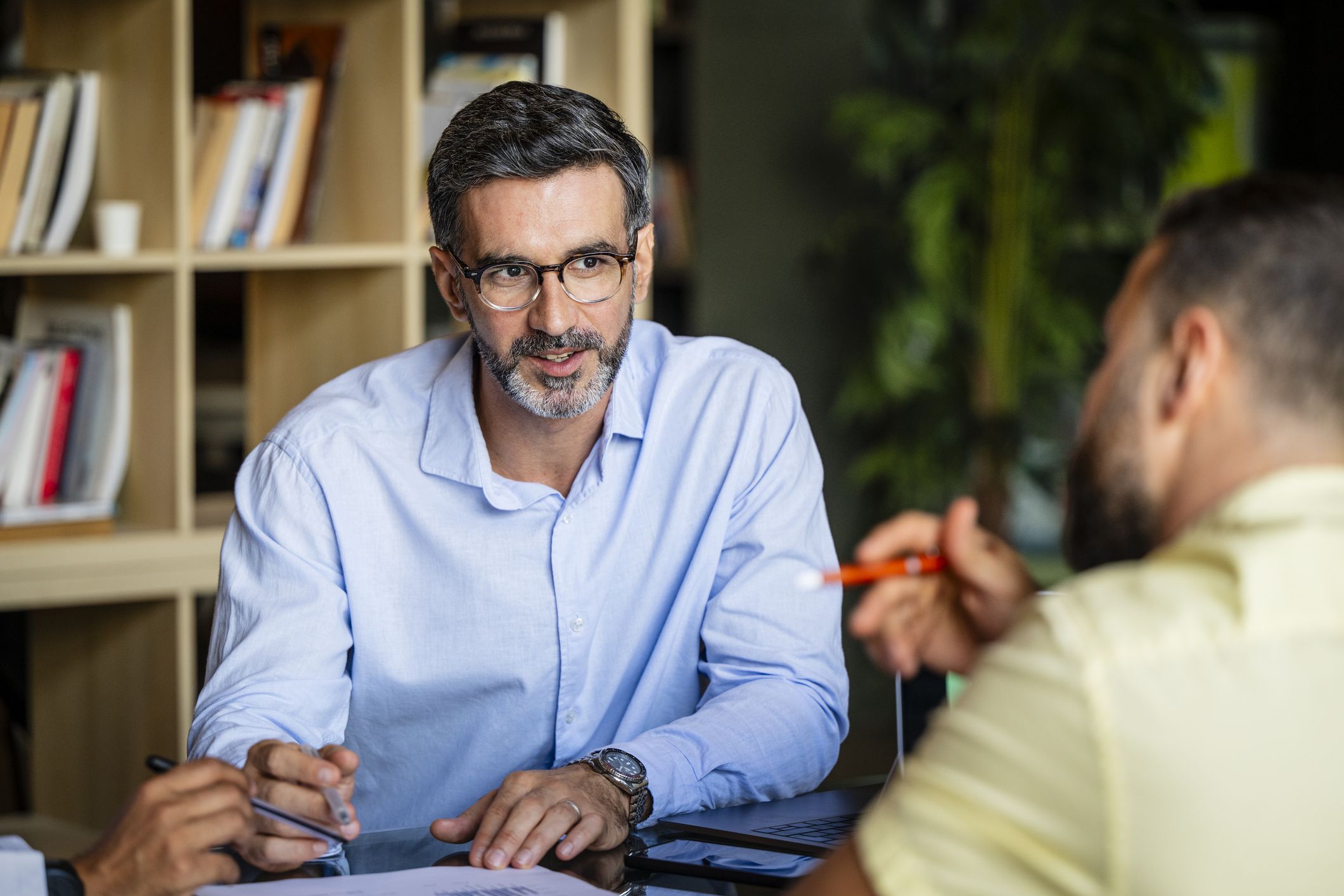 Man in a meeting, speaking and holding a pen