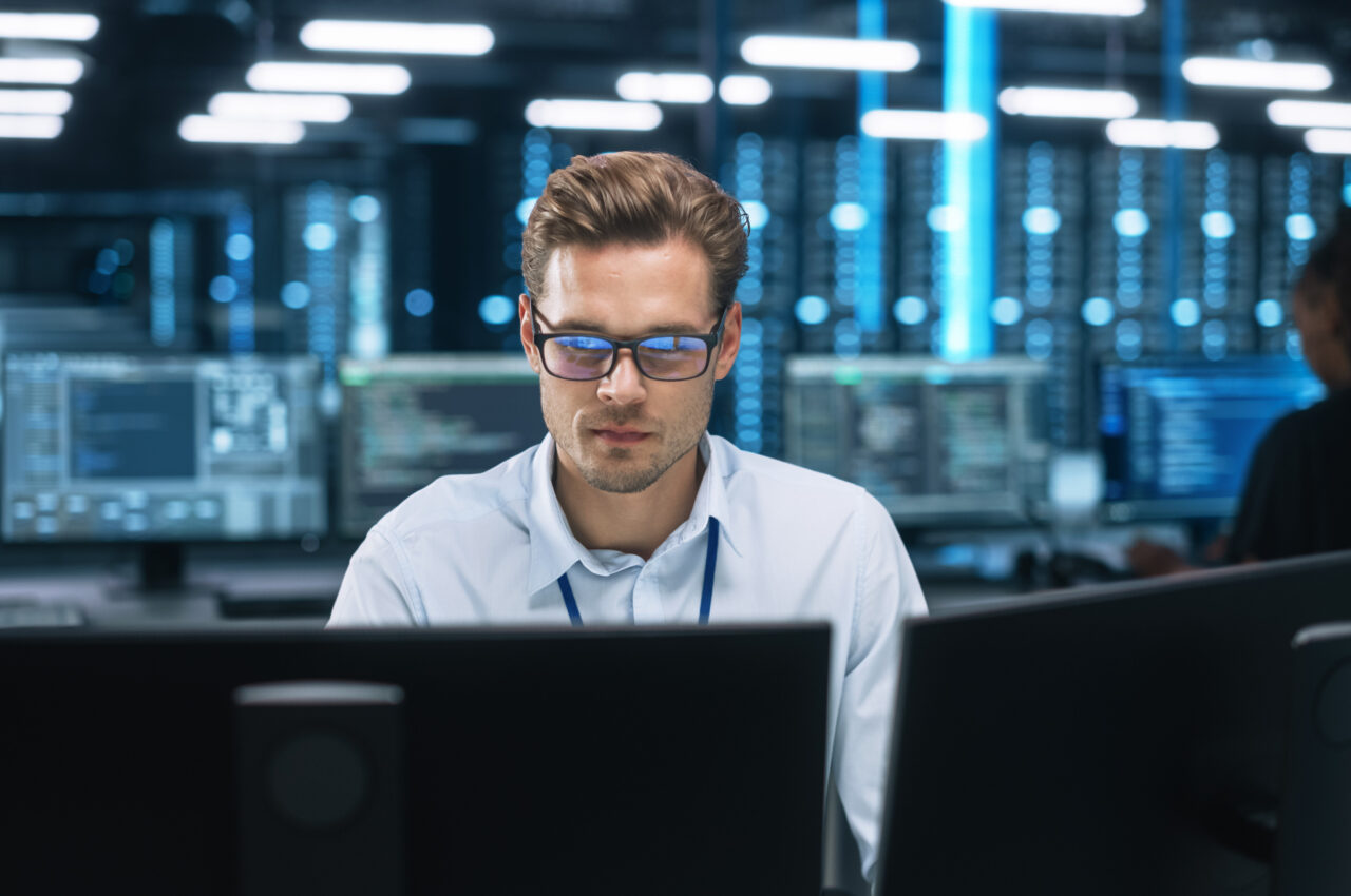 Man focused on computer monitors in a dimly lit server room