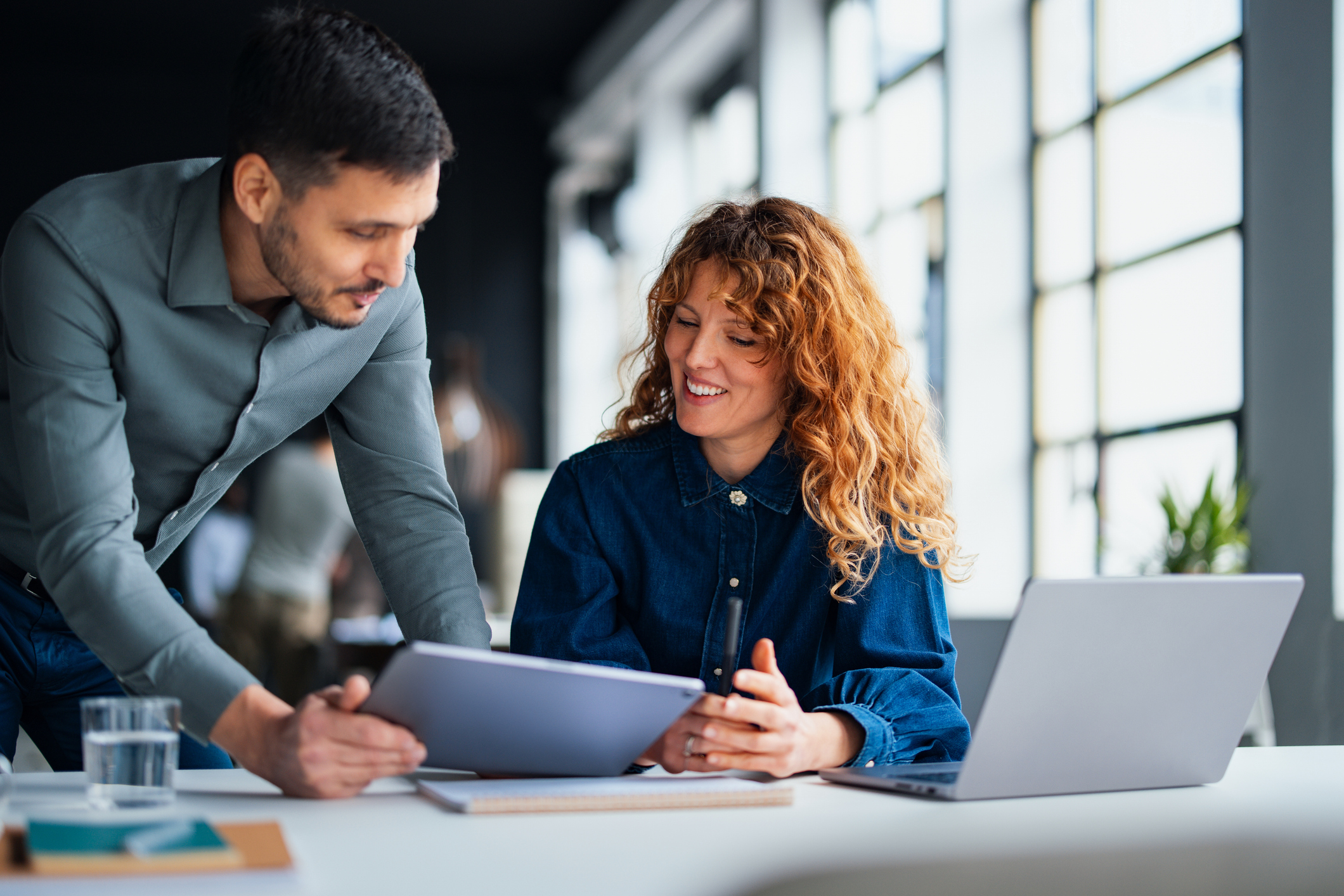 Colleague sharing tablet content with a smiling coworker in a bright office setting